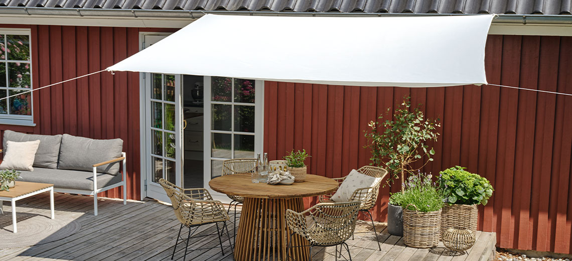 Grande voile d'ombrage en coloris blanc au-dessus d'une terrasse avec table et chaises de jardin