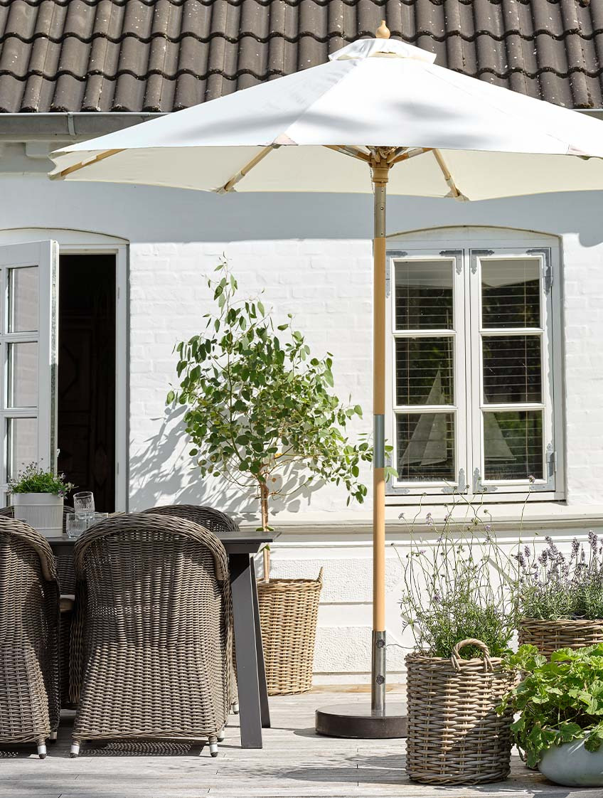 Parasol de jardin classique coloris blanc cassé sur une terrasse avec table et chaises de jardin